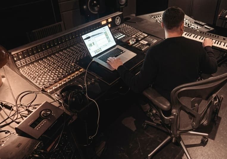 Musikproducent arbetar med laptop, mixerbord och keyboard i studio